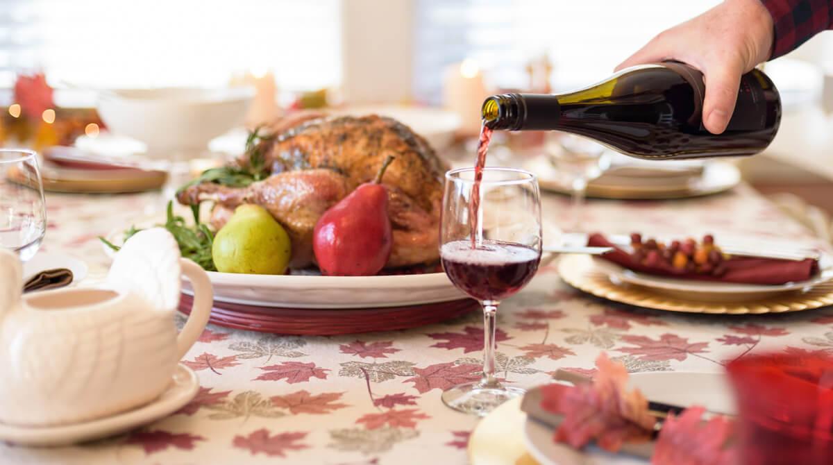 Mesa de reifeição cheia de alimentos e homem serve vinho em uma taça.