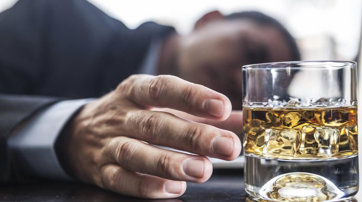 Homem deitado em uma mesa segurando um copo de whisky.