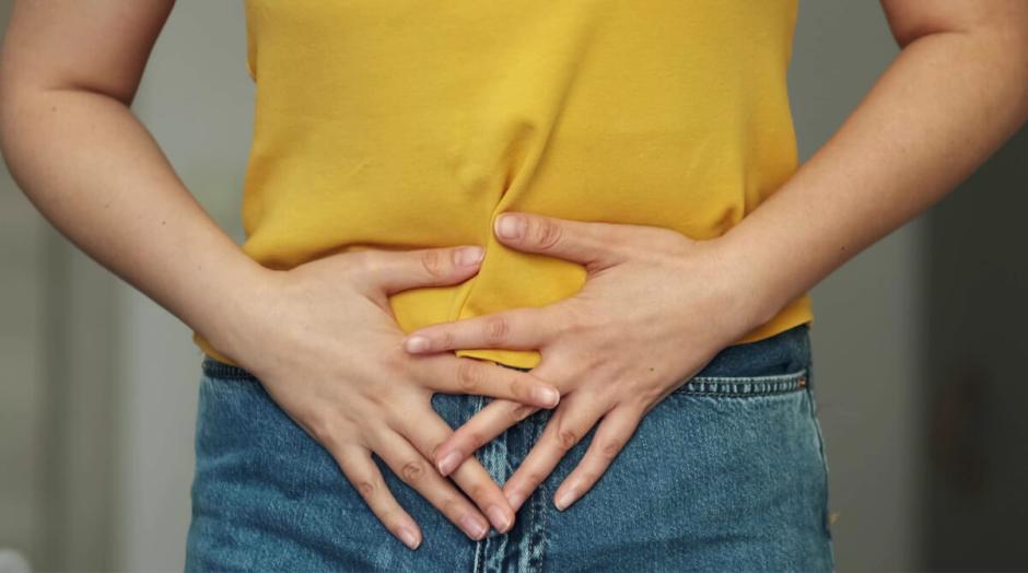 Mulher segura barriga por causa de dor.
